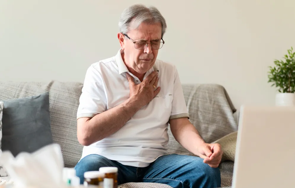 Hombre sentado en su sala con dolor fuerte en el pecho debido a un ataque cardiaco