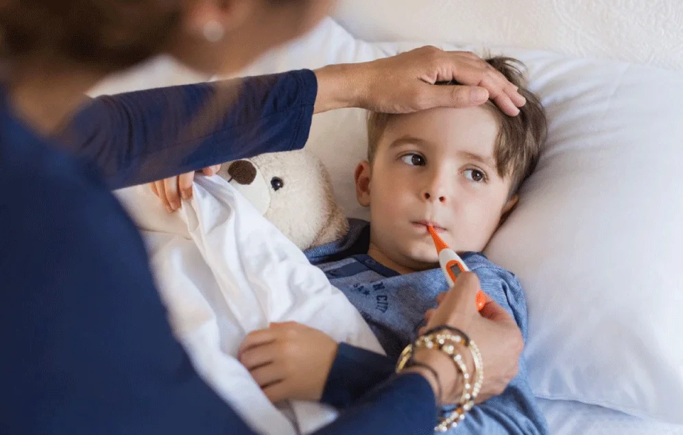 Mujer le está tomando la temperatura a su hijo, debido a que presenta dolor de cabeza y puede ser un signo de alarma ante la taquicardia.