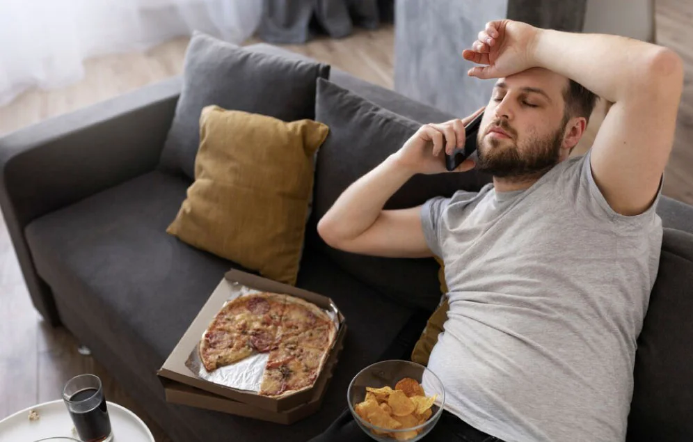 Hombre sentado en su sofá, comiendo comida chatarra, teniendo una vida sedentaria