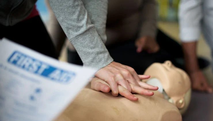 muestra a una persona practicando compresiones torácicas en un maniquí de RCP. Se enfoca en las manos entrelazadas de la persona sobre el pecho del maniquí.