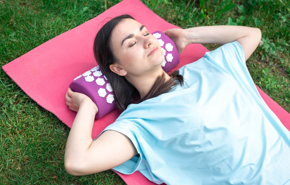 Una mujer relajada yace sobre una esterilla y almohada de acupresión. Esta práctica ayuda a reducir el estrés, lo cual es beneficioso para la salud cardiovascular